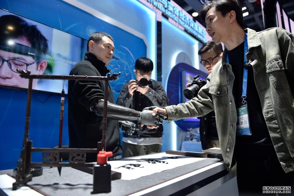 在第二届全球数字贸易博览会上，观众体验与穿戴智能仿生手的参展人员握手。新华社记者刘岭逸 摄