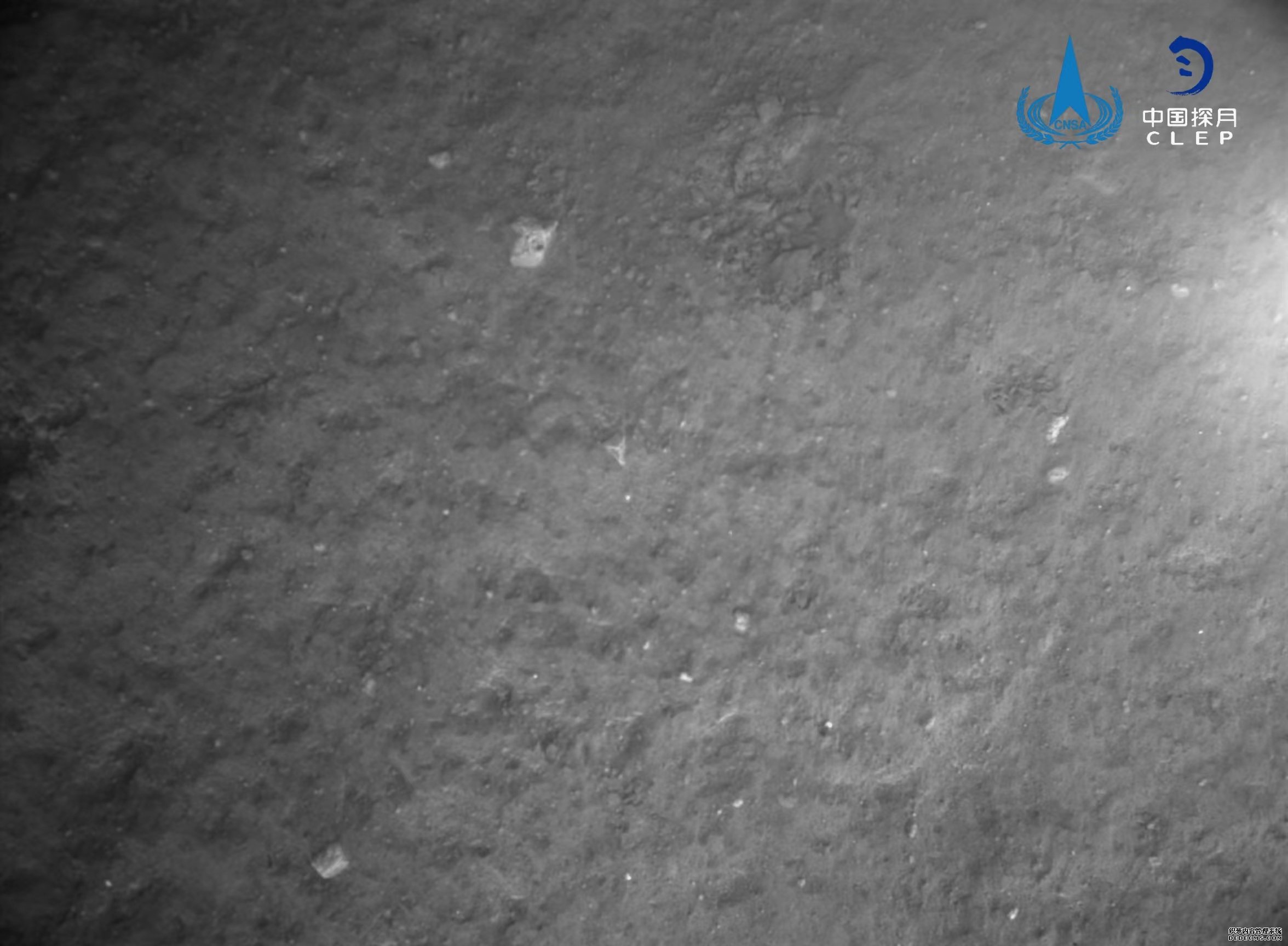 该图由降落相机在着陆器安全着陆后拍摄，图像显示着陆器底部相对平坦，分布有少量亮色石块。